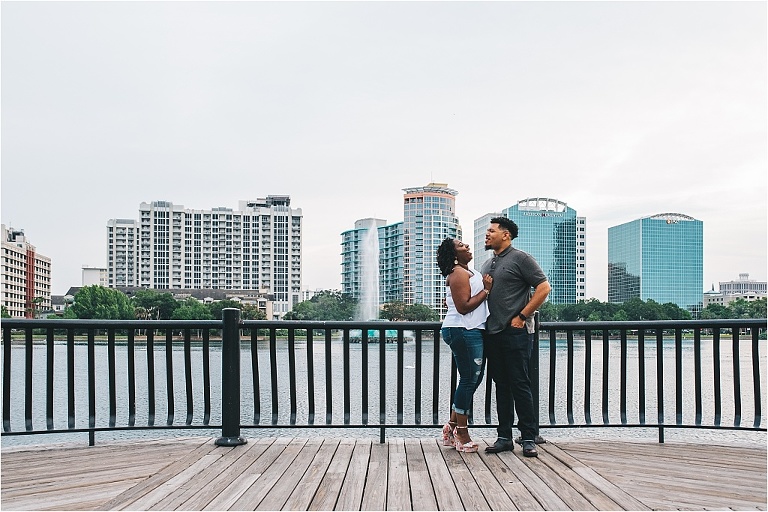couple having an adorable moment with the downtown orlando cityscape in the background during a sweet engagement session next to lake eola
