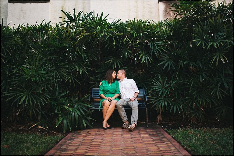 couple sitting on bench about to kiss during engagement photos near chapel at rollins college winter park fl