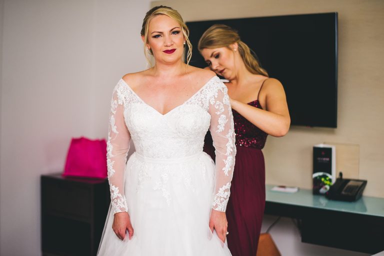maid of honor helping bride put on dress